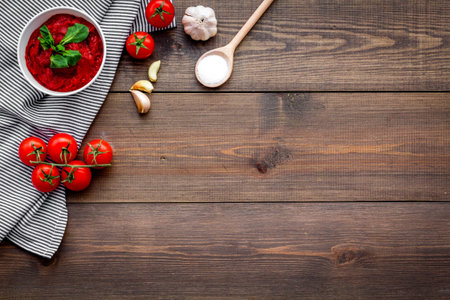Homemade tomato ketchup with cherry tomatoes, garlic and basil on dark wooden background top view.