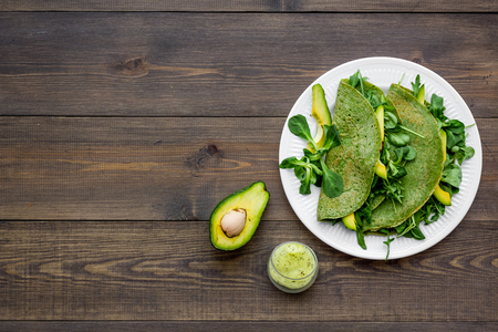 Healthy vegetable pancake. Spinach pancakes served with cucumber, avocado and greenery on dark wooden background top view.の写真素材