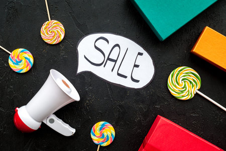 Sale concept with megaphone. Declare the sale. Electronic megaphone near word sale in cloud, gift boxes and sweets on black background top view.の写真素材