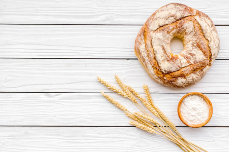 Home bread with classic recipe. Round loaf near ears of wheat on white wooden background top view.