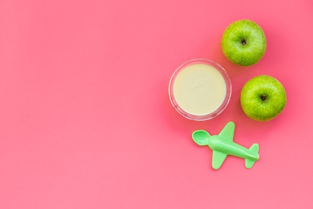 Healthy food for little baby. Apple puree with near toys on pink background top view.の写真素材