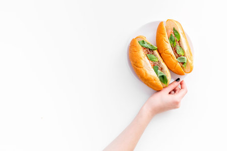 Hand takes homemade hot dogs with grilled sausages and greenery on white background top view.の写真素材