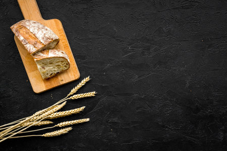 Homemade fresh bread sliced on cutting board on black background top view copy space