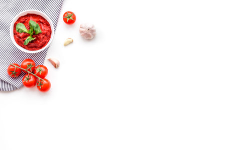 Ingredients for tomato sauce. Cherry tomatoes, garlic, green basil, black pepper, salt in spoon on white background top view space for text