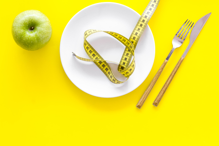 Proper nutrition with dietary fibre for weight loss. Apple on plate near measuring tape on yellow background top view copy spaceの写真素材