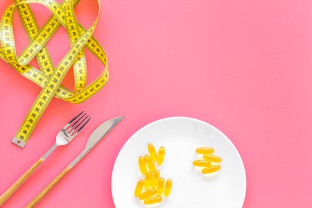 Pills or dietary supplement for weight loss. Treatment of obesity. Treatment of anorexia. Gold pills on plate near measuring tape on pink background top view copy spaceの写真素材