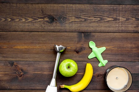 Homemade baby food. Cook puree with apple and banana with immersion blender. Dark wooden background with toy top view space for textの写真素材