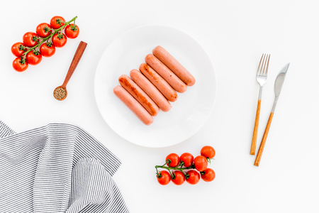 Grilled sausages on white table near cherry tomatoes and spices in wooden spoons top viewの写真素材