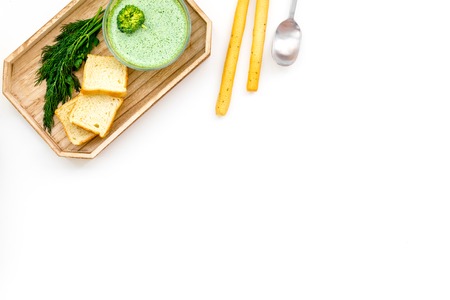 Green broccoli cream soup with broccoli served with rusks and greens on white background top view.の写真素材