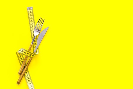 Diet, weight loss, slimming concept. Fork and knife with wound measuring tape on yellow background top view.の写真素材