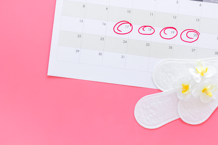 Menstruation cycle concept. Menstruation calendar with sanitary pads and flowers on pink background top view copy spaceの写真素材