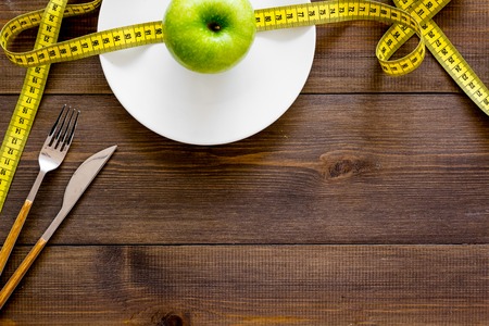 Proper nutrition with dietary fibre for weight loss. Apple on plate near measuring tape on dark wooden background top view copy spaceの写真素材
