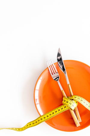 Diet for weight loss concept. Proper nutrition. Medical starvation. Empty plate with fork and knife near measuring tape on white background top view space for textの写真素材