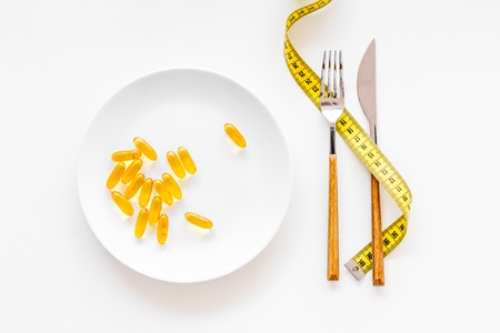 Dietary supplement for well-being. Fish oil or omega-3 capsules on plate near measuring tape on white background top viewの写真素材