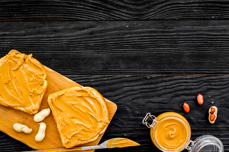 Make toast with nut paste. Two toasts, knife and glass jar with nut paste on black wooden background...