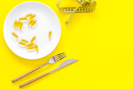 Dietary supplement for well-being. Fish oil or omega-3 capsules on plate near measuring tape on yellow background top view copy spaceの写真素材