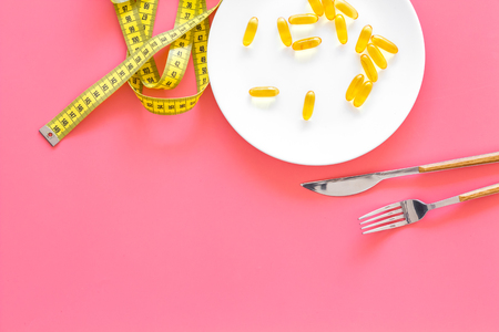 Medication and healthcare concept. Pills for treat diseases of stomach and intestines on plate near measuring tape on pink background top view copy spaceの写真素材