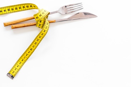 Diet, weight loss, slimming concept. Fork with wound measuring tape on white background top view.の写真素材