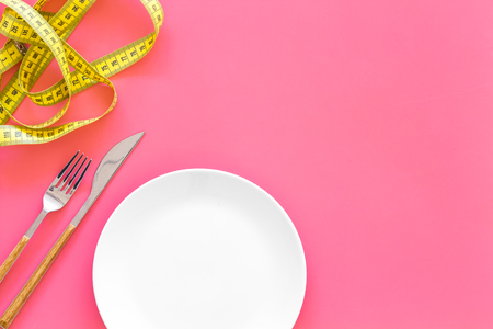 Diet for weight loss concept. Proper nutrition. Medical starvation. Empty plate with fork and knife near measuring tape on pink background top view.の写真素材