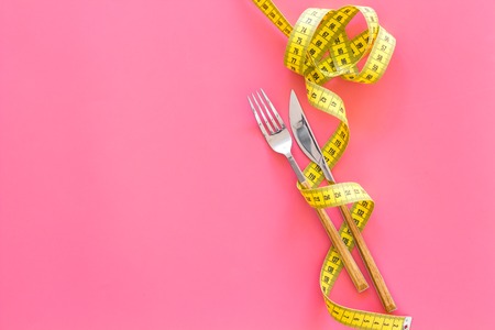 Proper nutrition for slimming. Fork and knife with wound measuring tape on pink background top view copy spaceの写真素材
