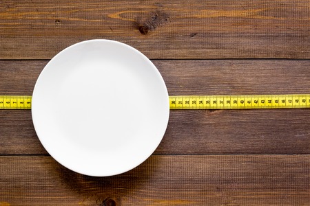 Proper nutrition for slimming. Empty plate and measuring tape on dark wooden background top view mockupの写真素材
