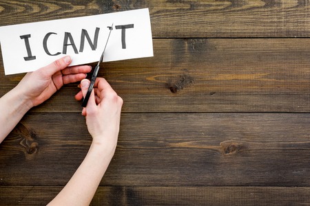 I can concept. Motivate yourself, believe in yourself. Hand cut off the letter t of written word I cant by scissors. Dark wooden background top view copy spaceの写真素材