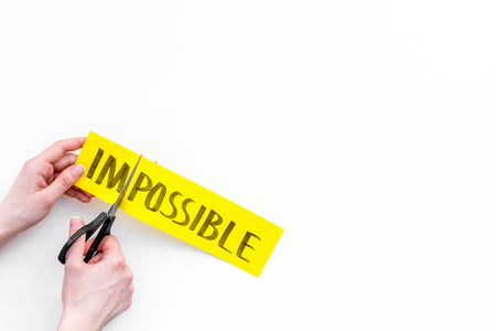 All is possible concept. Hands cutting the part im of written word impossible by scissors. White background top view.の写真素材