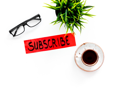 Email subscribe concept. Hand lettering subscribe on work desk with plant, glasses, cup of coffee on white background top view copy spaceの写真素材
