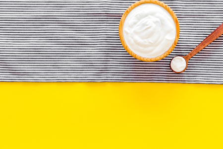 Food helps digestion. Greek yogurt in brown bowl near spoon on blue tablecloth, yellow background top view.の写真素材
