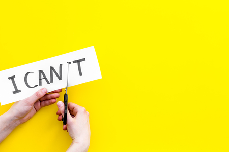 I can concept. Motivate yourself, believe in yourself. Hand cut off the letter t of written word I can't by scissors. Yellow background top view.の写真素材