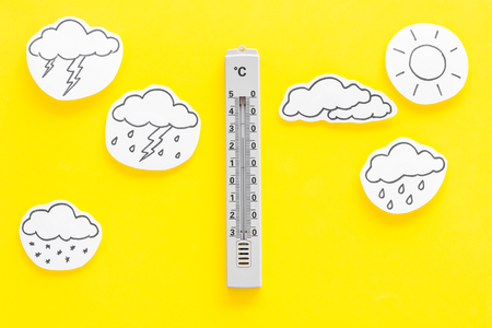 Weather forecast concept. Air temperature. Thermometer among cloud and lightening, sun, rainy clouds on yellow background top view.の写真素材