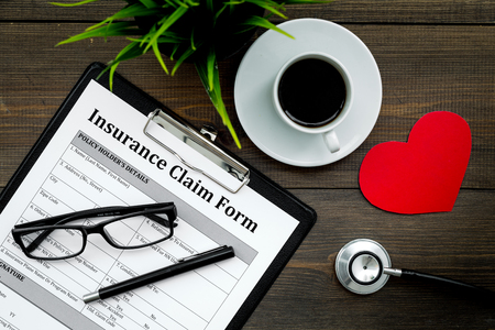Health insurance claim form for fill out. Empty form near heart sign and stethoscope on dark wooden background top view.の写真素材