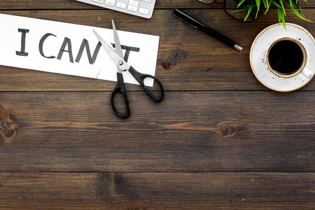 Self-doubt concept. Fight against self-doubt. Scissors close the letter t of written word I cant. Office desk. Dark wooden background top view space for textの写真素材