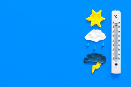 Weather forecast concept. Air temperature. Thermometer among cloud and lightening, sun, rainy clouds on blue background top view copy spaceの写真素材