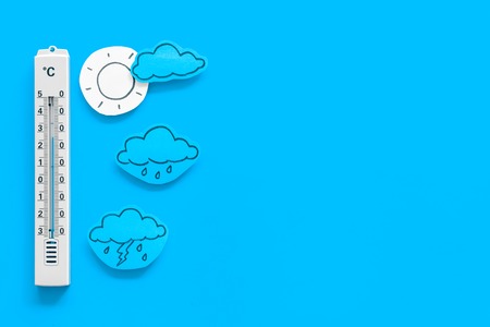 Weather forecast concept. Air temperature. Thermometer among cloud and lightening, sun, rainy clouds on blue background top view copy spaceの写真素材