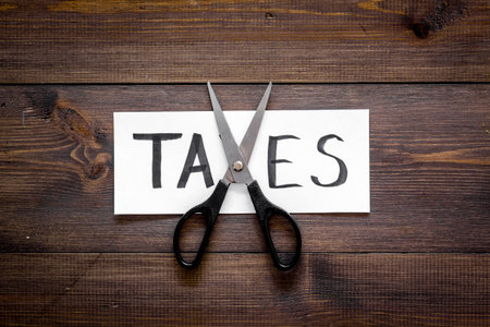 Cut taxes concept. Scissors cut paper with word Taxes on dark wooden background top view copy spaceの写真素材