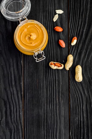 Peanut butter in glass jar near peanut on black wooden background top view copy spaceの写真素材