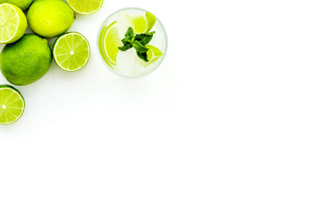 Refreshing mojito cocktail. Slices of lime, mint, glass with ice cubes on white background top view...