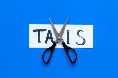 Cut taxes concept. Scissors cut paper with word Taxes on blue background top view space for textの写真素材