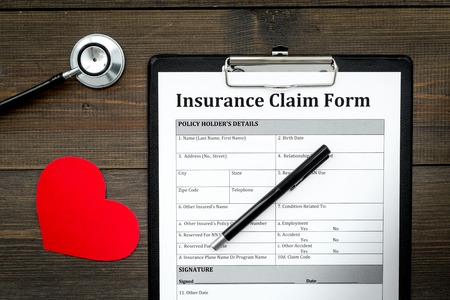 Health insurance claim form for fill out. Empty form near heart sign and stethoscope on dark wooden background top viewの写真素材