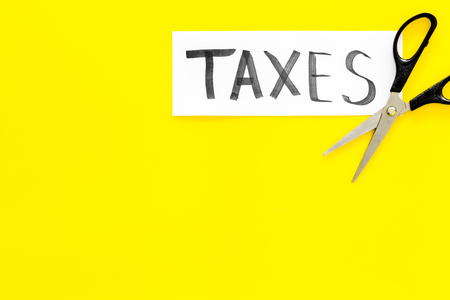 Cut taxes concept. Scissors cut paper with word Taxes on yellow background top view space for textの写真素材