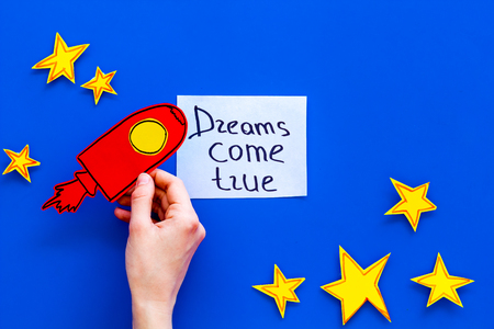 Motivational poster. Dreams come true hand lettering at blue cosmos background with rocket and stars top view copy spaceの写真素材
