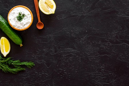 Greek yogurt dip with greenery, cucumber, oranges, garlic on black background top view copy spaceの写真素材