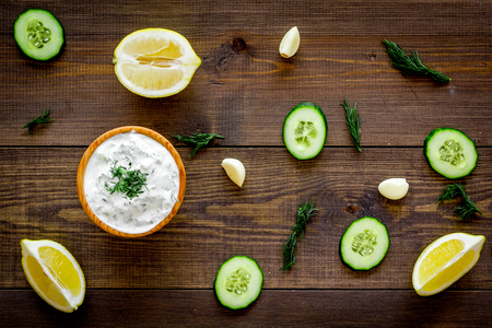 Greek yogurt dip with greenery, cucumber, oranges, garlic on dark wooden background top view.の写真素材