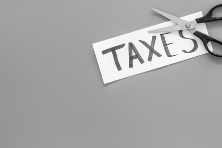 Cut taxes concept. Scissors cut paper with word Taxes on grey background top view.の写真素材