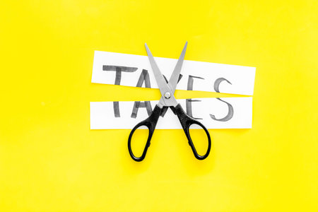 Cut taxes concept. Scissors cut paper with word Taxes on yellow background top view.