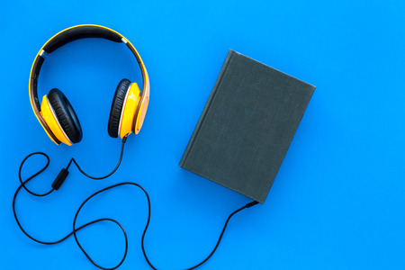 Audiobooks concept. Headphones connected with hardback book with empty cover on blue background top view copy spaceの写真素材
