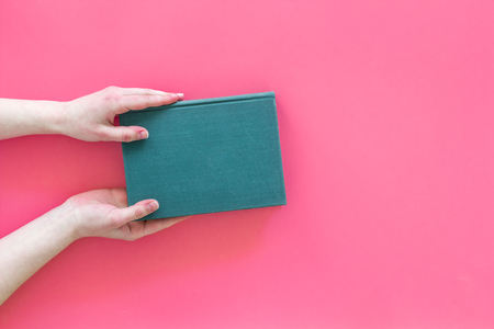 Reading concept. Reading as hobby. Hands take hardback book with empty cover on pink background top view copy spaceの写真素材