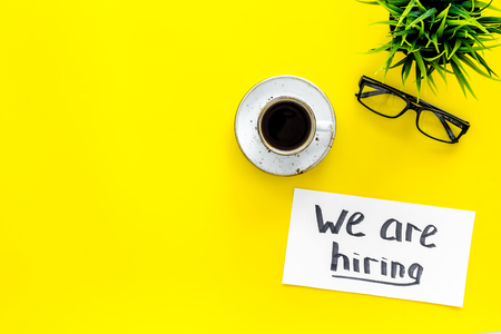 Search for worker, employee concept. We are hiring lettering on work desk on yellow background top view copy spaceの写真素材