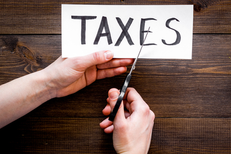 Tax reduce concept. Hands with scissors cut paper with word Taxes on dark wooden background top view copy spaceの写真素材